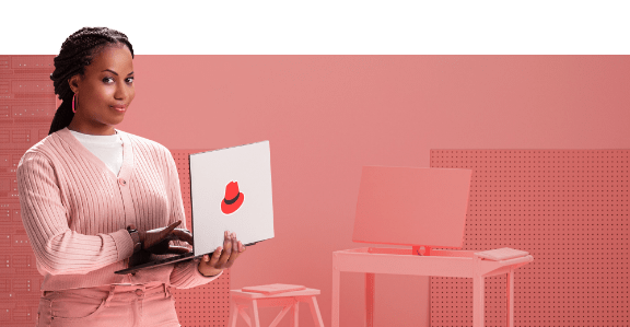 Eine Frau schaut von ihrem Laptop mit Red Hat-Logo auf und lächelt selbstbewusst.